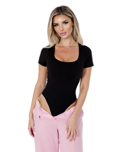 Model showcasing the Amara Top, a sleek black bodysuit paired with pink pants, highlighting its stylish design and fit.