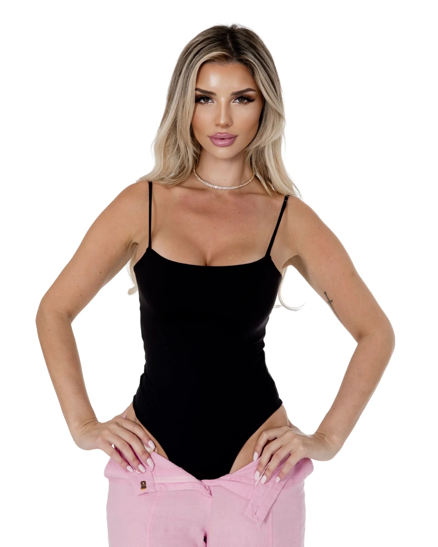 Model wearing the Elara Bodysuit in black, showcasing a stylish look with pink pants.